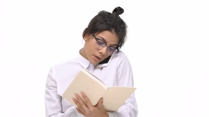 Sticker - Concentrated young business woman in glasses holding book while talking on mobile phone isolated