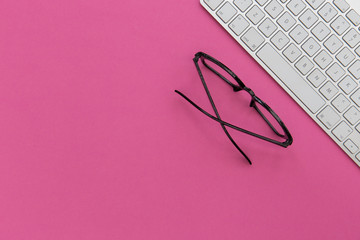 Wall Mural - reading glasses and computer keyboard on bright pink background