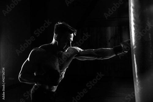 Foto Young male boxer hitting punching bag on black background.