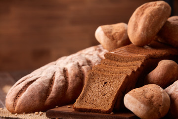 Freshly baked bread loaves on burlap on wooden table with brown blurred background. Texture closeup bakery products