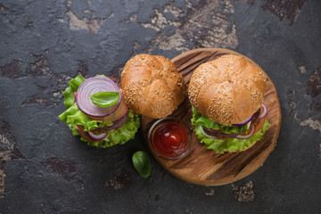 Top view of two double beef burgers with white sesame bun over dark brown stone background