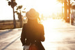 © WHstudio Leushin N - Back view of slender young woman wearing hat and coat walking down street on sunny spring day, heading to city beach to enjoy beautiful sunset. People, lifestyle, travel and vacations concept