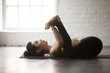 Young attractive yogi woman practicing yoga concept, lying in Happy Baby exercise, Ananda Balasana pose, working out, wearing black sportswear, full length, white loft studio background, side view