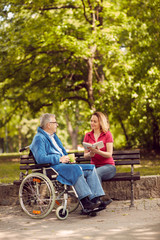 Wall Mural - Young carer woman reading book in the park disabled man in wheelchair.