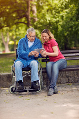 Wall Mural - Disabled retiree man in park using tablet with daughter.