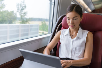 Businesswoman working on laptop on train. Asian freelance writer or designer writing emails on computer while commuting to meeting in the city. Commuter woman urban travel.