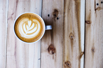 Wall Mural - Latte art coffee in white mug on wood table in coffee shop.