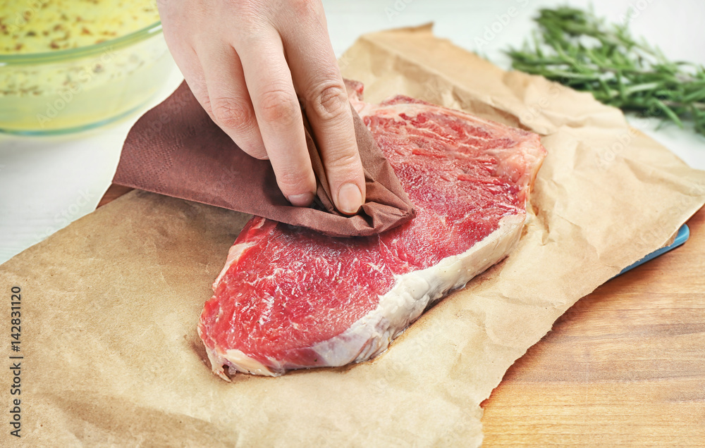 Female hand preparing raw steak on wooden board with parchment
