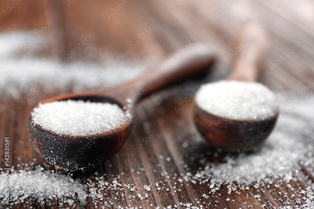White sand sugar in spoons on wooden background