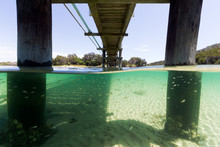 Small Fish School Together Under A Pier In Turquoise Water In This Underwater Split Image Taken In Australia.