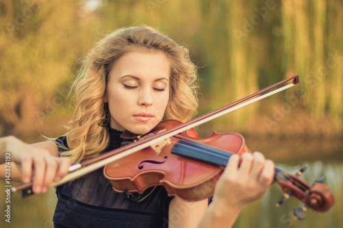 Plakat Młoda kobieta bawić się skrzypce przy parkiem. Niewielka głębokość pola.