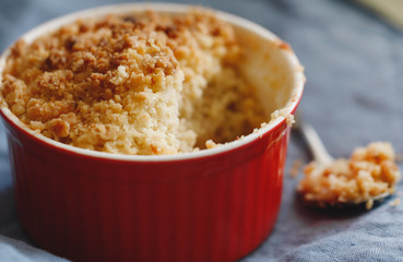 Close-up of an apple crumble pie in a red bowl on a blue napkin. Macro photography.