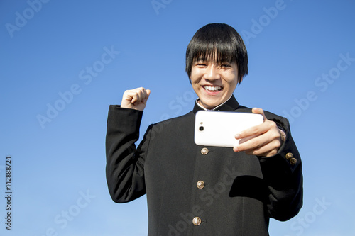 スマホを見ながらガッツポーズの制服姿の男子高校生 Stock Photo Adobe Stock