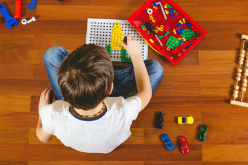 Child playing with toys tool kit while sitting on the floor in his room.Top view