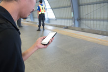 Businessman Using The Smart Phone On Abstract Blurred Photo Of Sky Train At Station With Security Guard