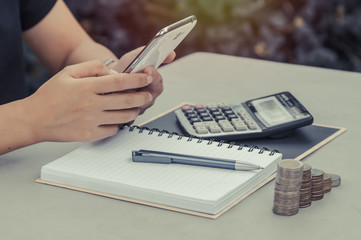women use phone with book, calculator and coins on table