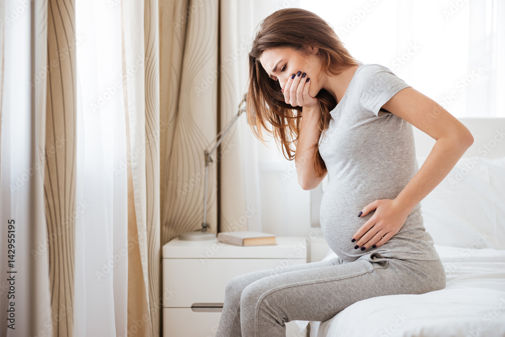 Pregnant young woman sitting on bed and feeling sick - obrazy, fototapety, plakaty 