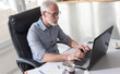 © thodonal - Portrait of senior businessman working on laptop, hard light