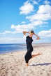 © raisondtre - Wonderful portrait of a young slim woman in a black dress with a white Bolero, dancing barefoot on sand, on a background of blue sky and white clouds of air.