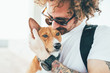 © onewithahalf - Young trendy hipster with tattoos crazy curly hair with his best friend a cute small basenji puppy gives him a tender kiss on ears while hugs him with his arms