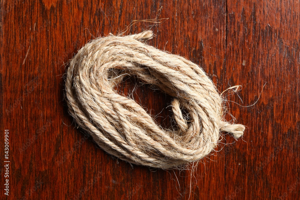 A coil of brown manila rope cable in normal light put on the dark brown ...