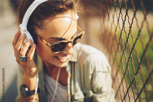 Fotografia Happy young woman listening to music via headphones on the street on a sunny day