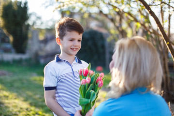 Wall Mural - Little boy surprise mother with tulips outdoor, Mother's day