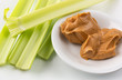 Celery stalks on a white plate with peanut butter to the side in a small bowl.
