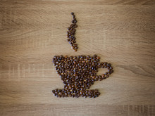 Shape Of Coffee Cup With Roasted Grains Over Wooden Background