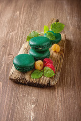 Traditional French sweets. A green makorunas with mint, white and red raspberries, blueberries on a wooden board. Dark background.