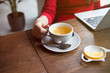© veera - Cropped view of female hand holding smart phone with blank screen for your text. Woman reading messages on cell phone with cafe interior background while drinking hot cup of tea with lemon