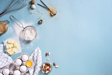 Healthy baking ingredients - flour, almond nuts, butter, eggs, biscuits over a blue table background. Bakery background frame. Top view, copy space.