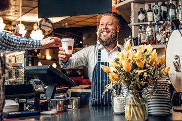 A man selling coffee to a consumer in a coffee shop.