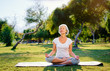 © luengo_ua - Yoga at park. Middle age woman in lotus pose sitting on green grass. Concept of calm and meditation.