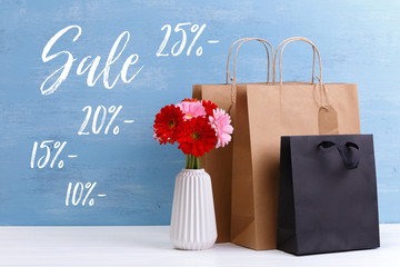 Wall Mural - Mockup of blank shopping bags. Sale discounts. Gerbera flowers in vase. Brown and black craft packages. Concept for sales or discounts. Blue wooden rustic board.