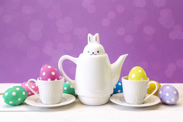 Kettle-hare with cups and Easter eggs on purple background.