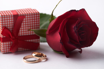 Closeup of Two gold wedding rings with pink gift box and wedding bouquet of red roses on isolated white background. Love and marriage proposal concept