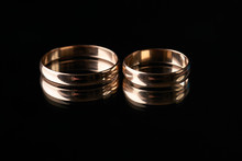 Closeup Of Two Classical Gold Wedding Rings On Isolated Black Mirror Background  On A Wedding Day. Love And Marriage Proposal Concept.