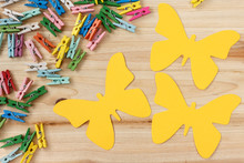 Yellow Cardboard Butterflies With Copy Space And Colorful Mini Clothespins On A Wooden Background