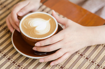 Close up of female hands holding cup of coffee on wooden table background