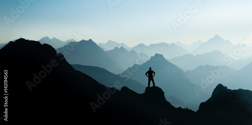 Fototapete Spectacular mountain ranges silhouettes. Man reaching summit enjoying freedom.