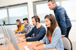 © W PRODUCTION - group of young people with desktop computer in row and headset training with teacher instructor in customer service call support helpline business center