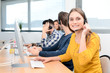 © W PRODUCTION - portrait of beautiful and cheerful young woman telephone operator with headset working on desktop computer in row in customer service call support helpline business center
