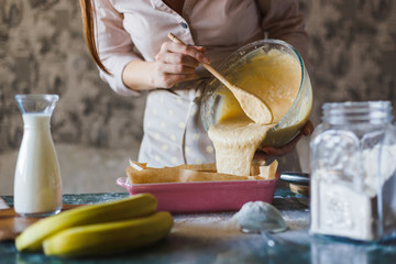 A young woman baker is pouring the dough into a baking dish.