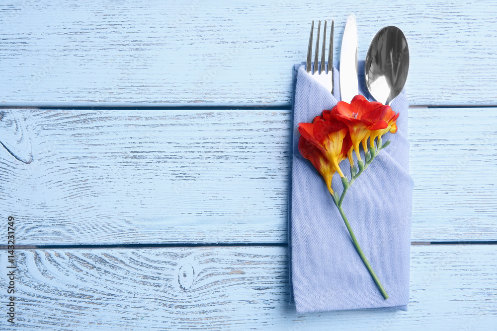 Cutlery set with folded napkin and flower on wooden table