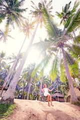 Wall Mural - Vacation concept. Happy young woman in white dress swinging at palm grove.