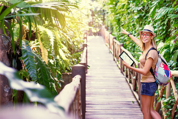 Wall Mural - Traveling concept. Technology and adventure. Young woman using tablet computer in jungle.