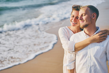 Love and romance. Honeymoon on the sea shore. Beautiful loving couple in white cloth embracing on the beach.