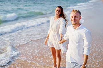 Wall Mural - Romantic dating. Young loving couple walking together by the sand beach enjoying sea