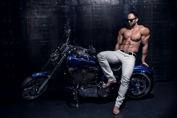 Sexy rich handsome attractive sporty muscular shirtless bodybuilder and fitness model with perfect torso body in white jeans sits on a beautiful blue shiny luxury motorcycle